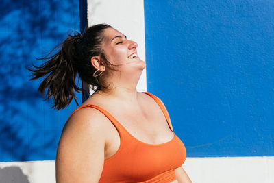 Cheerful plump ethnic sportswoman in active wear with flying hair having fun on sunny day