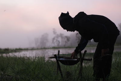 Man standing on field by lake against sky during sunset