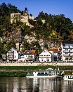 Buildings by river against trees