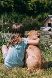 Friendship of animals and children, people.girl sits on the bank of a pond and hugs a labrador puppy