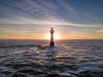 Lighthouse by sea against sky during sunset