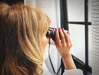 Woman looking through binoculars by window at home