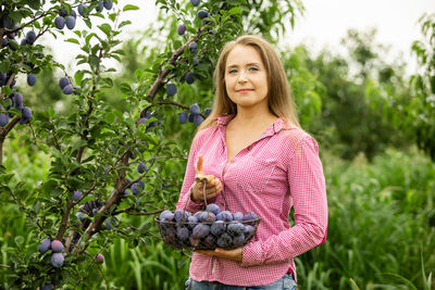 Young woman holding fruit against plants