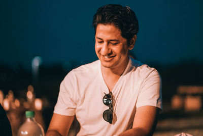 Close-up of smiling young man sitting against sky at night