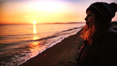 Young woman looking from coast away at sunset over the sea 