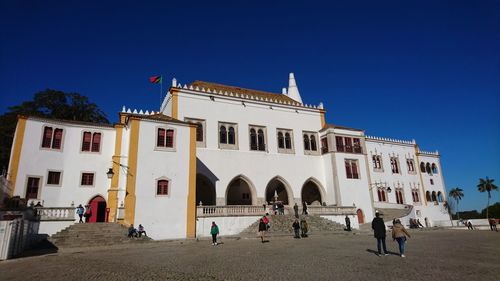 People in front of historic building against clear blue sky