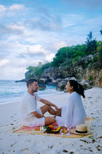 Rear view of couple sitting on beach against sky