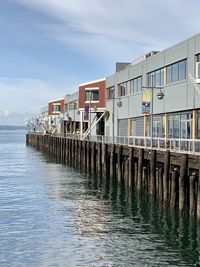 Wooden posts in sea by houses against sky