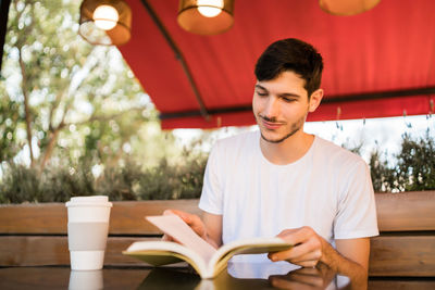 Young man reading book sitting at cafe