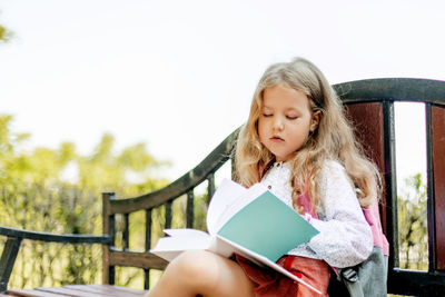 A cute thoughtful schoolgirl is sitting on a bench with books. back to school, lesson schedule