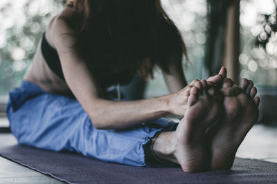 Low section of woman stretching while sitting on floor at home