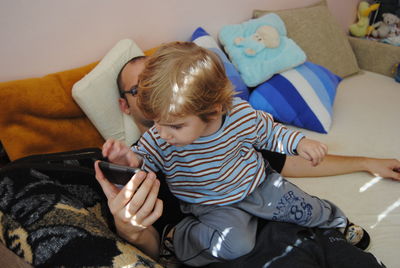Rear view of boy using mobile phone while sitting on father at home