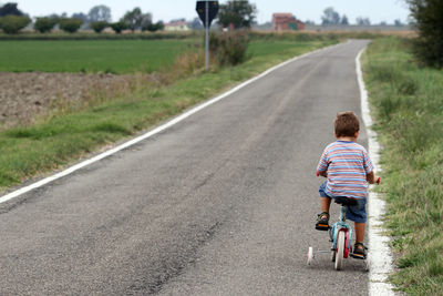 Rear view of boy riding bicycle on road