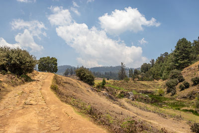 Dirt road amidst landscape against sky