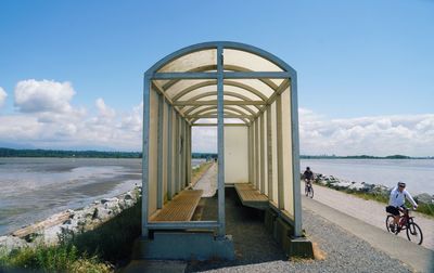 People riding bicycle on road by sea against sky