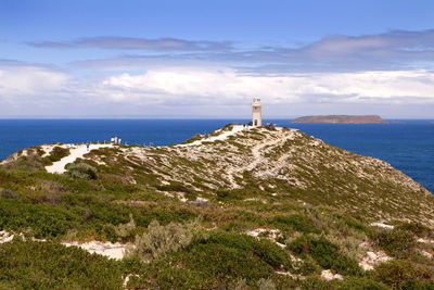 Lighthouse amidst sea and buildings against sky