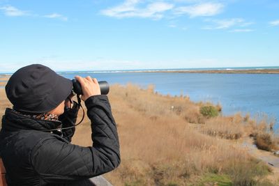 Side view of woman looking at sea through binoculars against sky