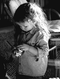 Cute girl holding flower while standing by chair