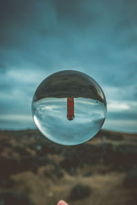 Close-up of crystal ball on landscape and tower reflection against blue sky