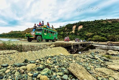 People on rocks by road against sky