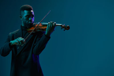 Low angle view of man playing violin against clear blue background