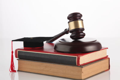 Close-up of hammer and gavel with books and mortarboard against white background