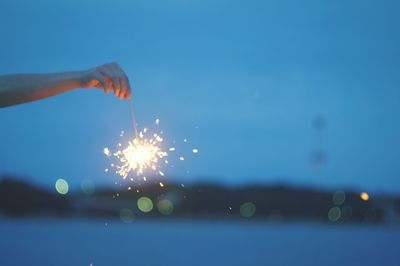 Close-up of hand holding sparkler against sky