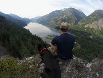 High angle view of man and black dog sitting on mountain against lake chelan