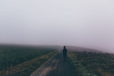 Rear view of woman walking on road against sky during foggy weather