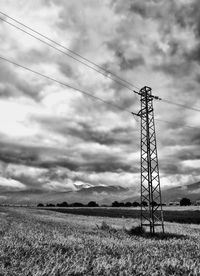 Electricity pylon on field against cloudy sky