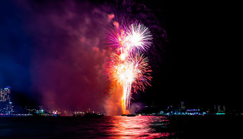 Firework display over illuminated city against sky at night