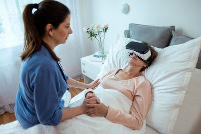 Side view of young woman holding camera on bed