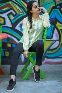 Full length of young woman sitting against graffiti wall on chair