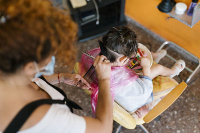 Hairdresser cutting wet hair of flittle girl searching clips in basket