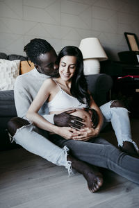 Affectionate man kissing pregnant woman sitting in living room at home