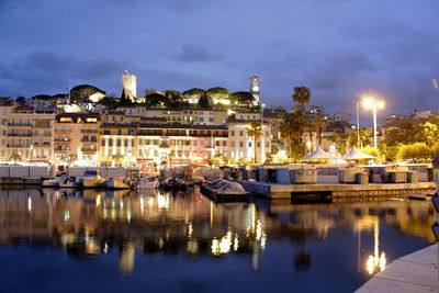 Boats moored at harbor by buildings against sky at dusk