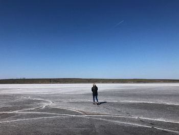 Rear view of man standing on land against clear blue sky