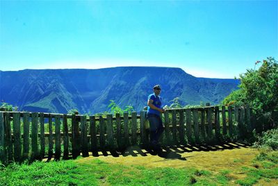 Rear view of man standing on mountain against clear blue sky