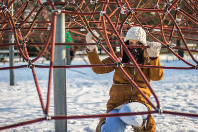 Portrait of woman crouching under ropes at snow covered park