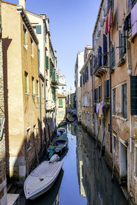 Boats moored in canal amidst buildings against clear sky