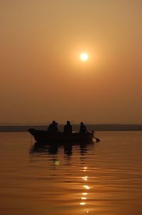 Silhouette people standing on sea against orange sky