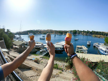 Cropped hands holding ice cream cone against harbor