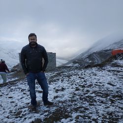 Full length portrait of young man standing in snowcapped mountain