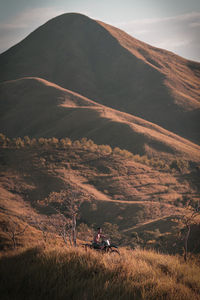 Man biking amidst field against mountain