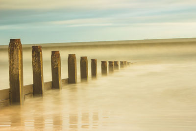 Wooden posts on beach against sky