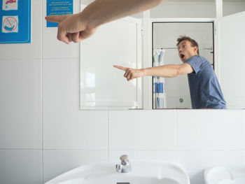 Shocked man gesturing at sign board while standing in bathroom