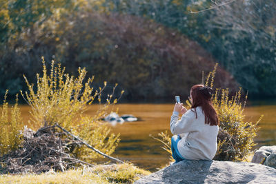 Woman sitting on a rock near the lake using her smartphone