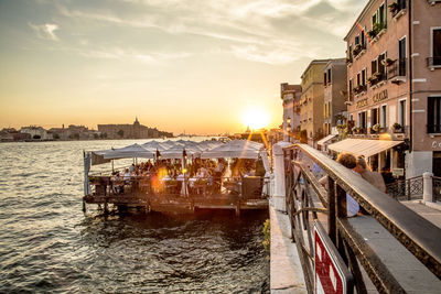 Canal amidst buildings in city against sky during sunset