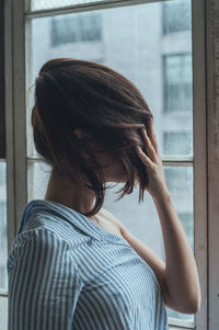 Close-up of woman covering face with hair against window