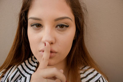 Close-up portrait of beautiful woman with finger on lips standing against brown wall